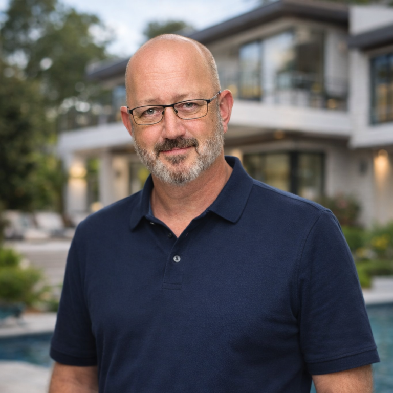 Mark Man in a navy polo shirt smiles in front of a modern house with greenery and pool.